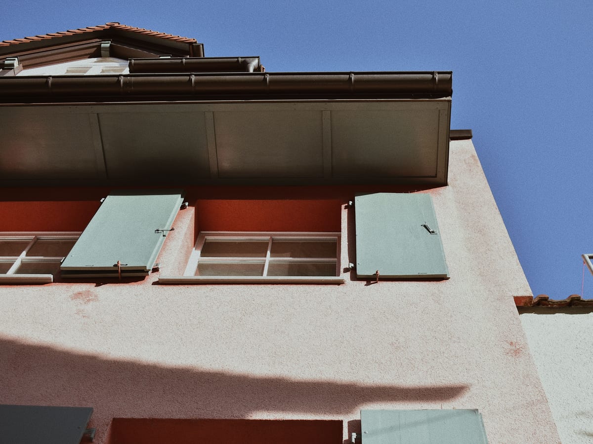 A close view of a building exterior showcasing distinctive green shutters against a pastel facade.